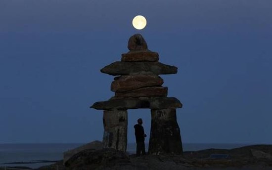 A man looks at a giant inukshuk as the moon rises above it in Rankin Inlet, Nunavut in this file photo from August 21, 2013.  PHOTO: CHRIS WATTIE/REUTERS