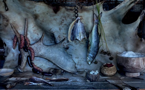 A spread of Arctic provisions including, from left, sun-dried white trout, moose antler, venison sausage, caribou blood sausage, dried Arctic flounder, dried sea bream, caribou lichen, meadow onion stems and seed heads, dried wild crowberries and geothermal Arctic sea salt against a deer hide backdrop.