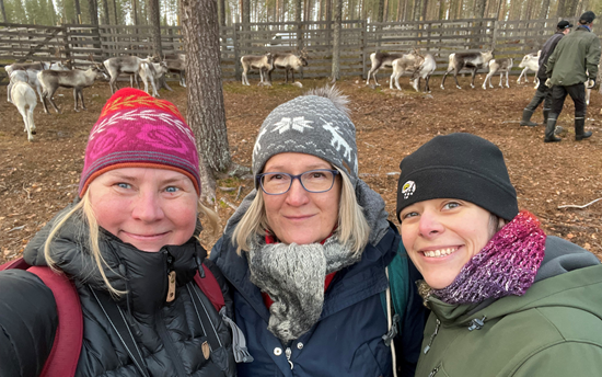 Image of Minna Turunen, Päivi Soppela, and Cara Ocobock with reindeer behind them.